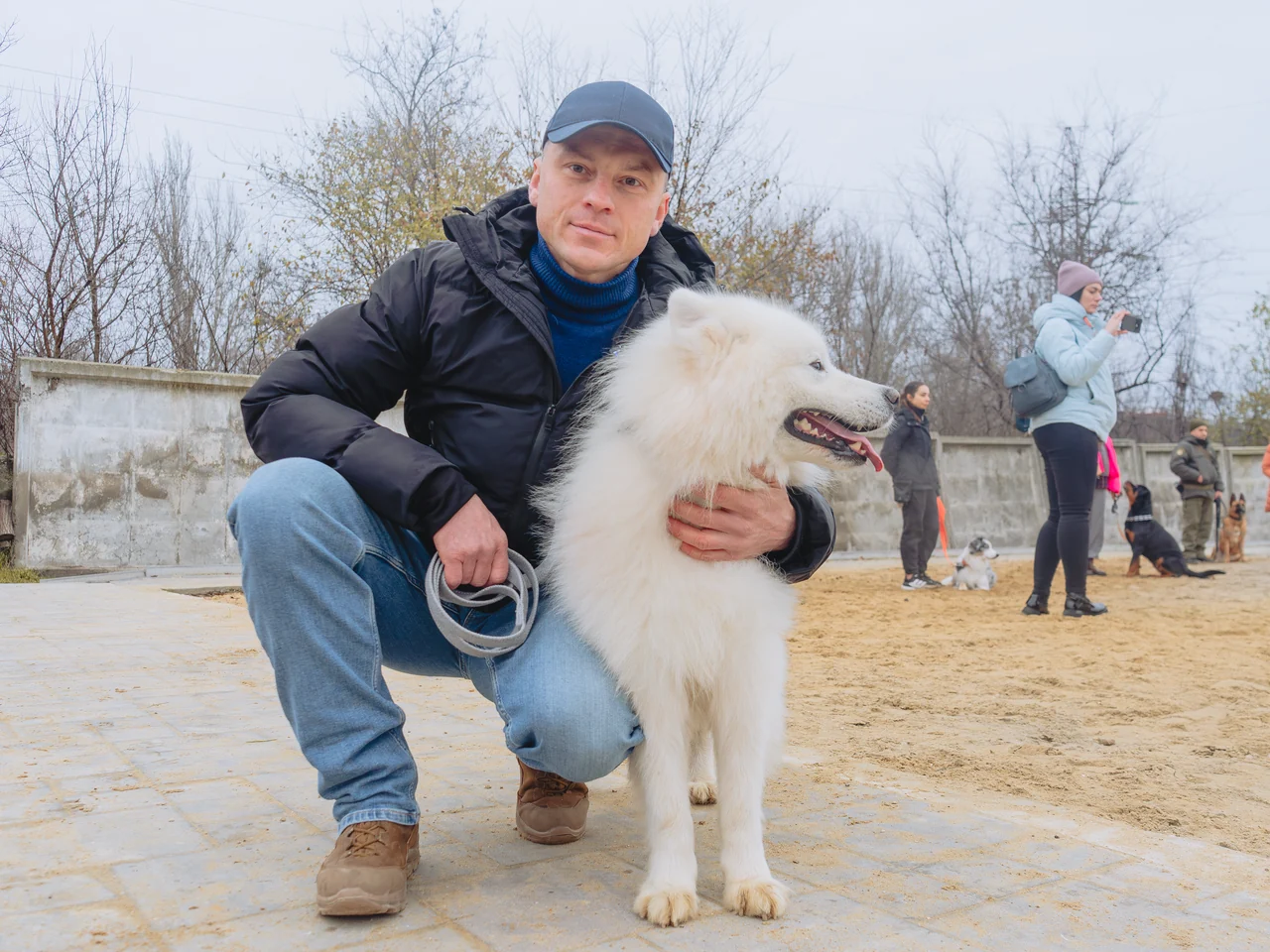 O participantă stă ghemuită lângă un câine alb pe terenul de antrenament al școlii