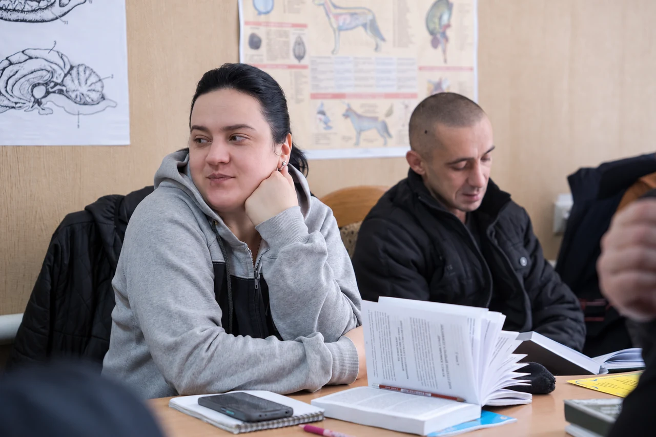 Participants sitting at a table with open books and notebooks in a classroom with canine anatomy posters
